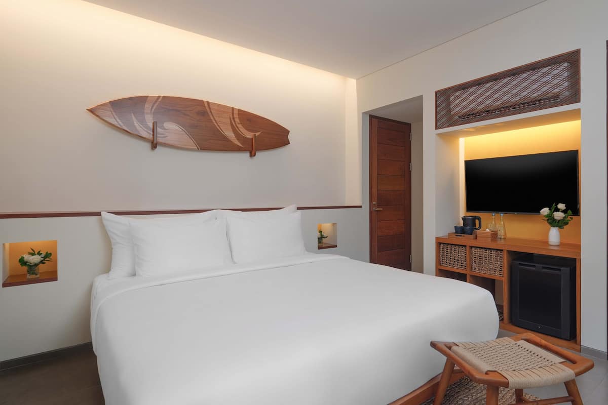 A hotel room with a large bed, a television, a wooden side table, and a wall-mounted surfboard decoration.