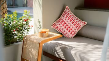 Una habitación con una cama, una mesita con una vela, un ventanal con vistas a la vegetación y un cojín estampado.