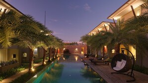 A swimming pool with lounge chairs and palm trees, surrounded by buildings with warm lighting. - Chesa Canggu (Canggu)