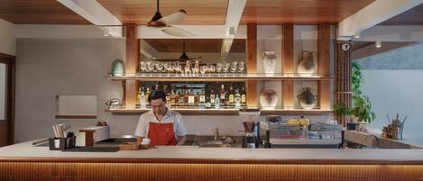 A bar area with a wooden ceiling, bar stools, and shelves with glasses and bottles.