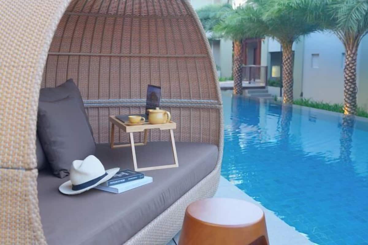 A cozy lounge area with a wicker sofa, a small table with a teapot, and a hat on the seat.