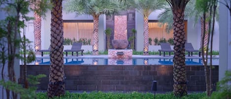 A pool area with lounge chairs, palm trees, and a stone wall.