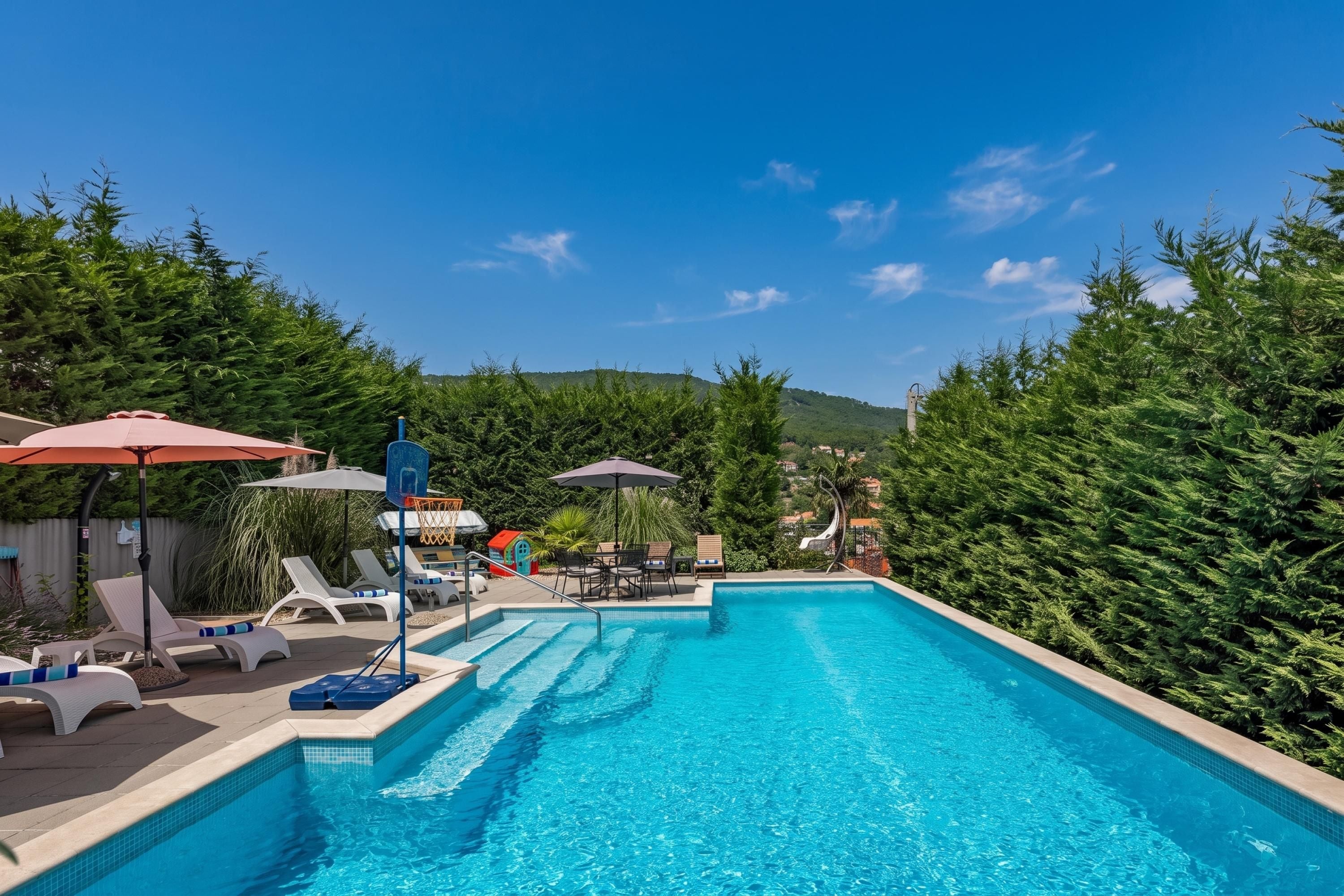 Una piscina con sillas de descanso y sombrillas, rodeada de vegetación y un cielo despejado.