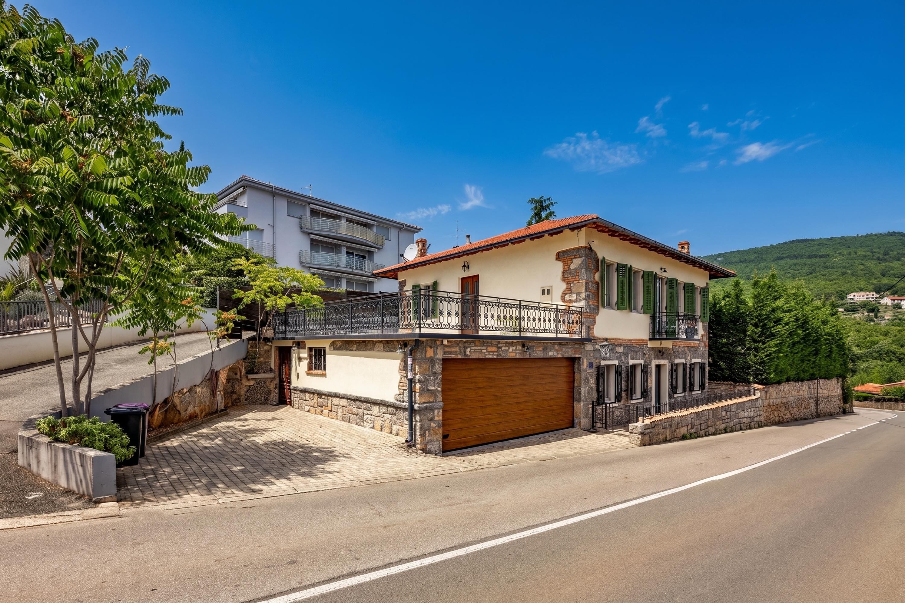 A two-story house with a stone facade, a wooden garage door, and a balcony with a metal railing.