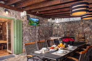 A dining area with a stone wall, wooden ceiling beams, and a television mounted above a fireplace. - Rustic Villa Okra With Pool (Opatija)