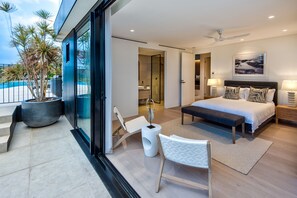 A modern bedroom with a large bed, bedside lamps, a bench, and a view of the outdoors.