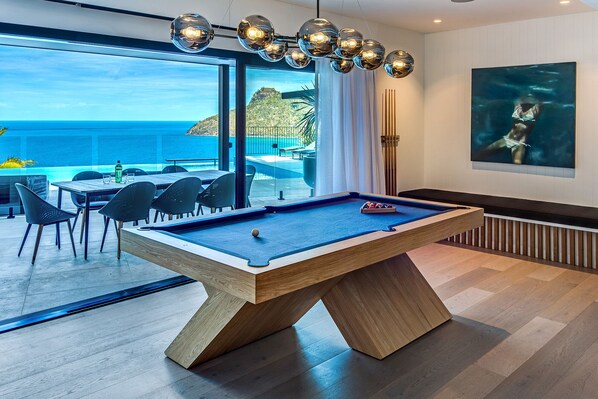 A pool table in a modern room with a view of the ocean.