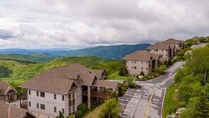 Een woonwijk met meerdere tweelaagse huizen, een verharde weg en een uitzicht op groene heuvels in de verte.