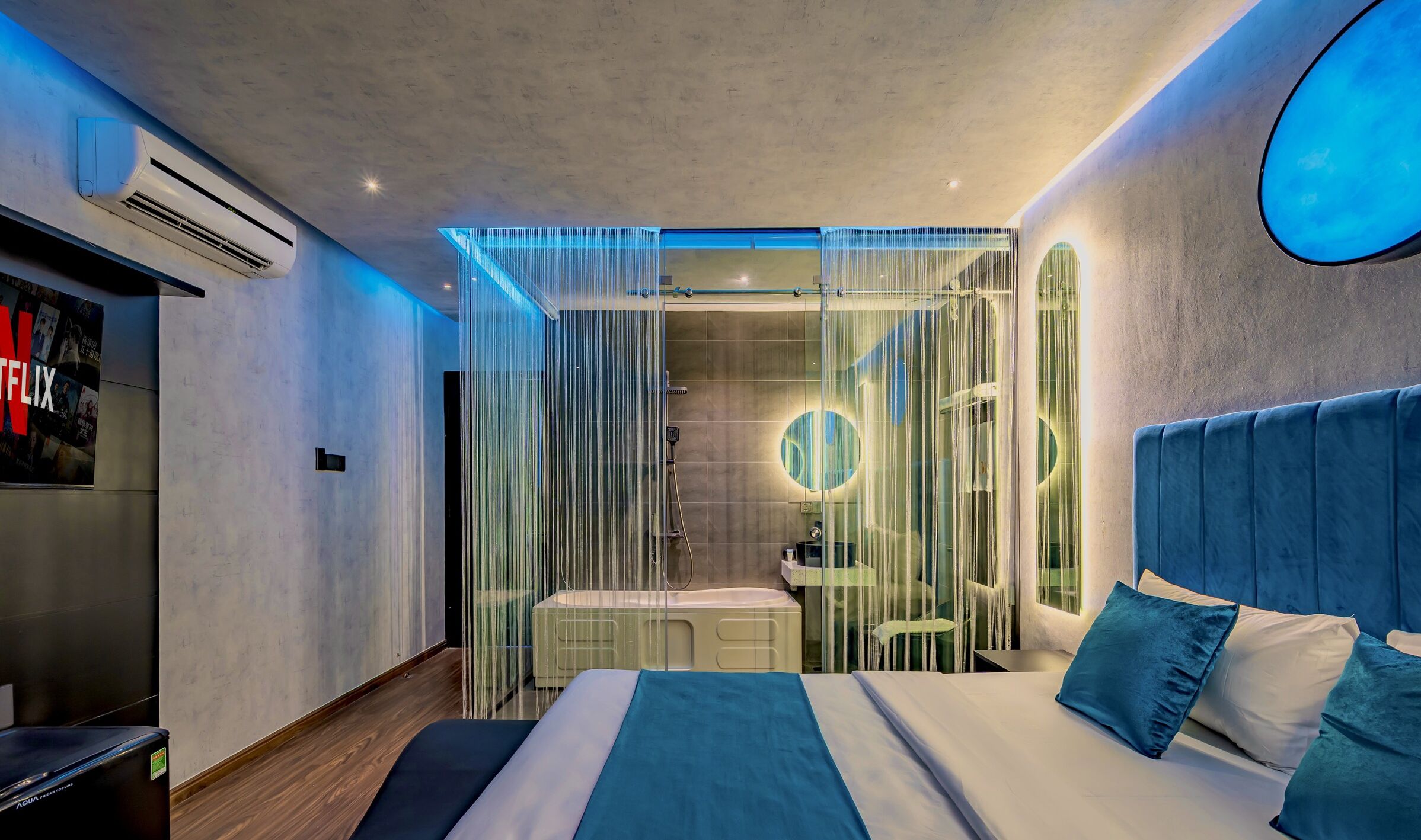 Una habitación de hotel moderna con una cama grande, televisión y zona de ducha.