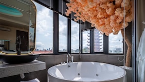 A modern bathroom with a freestanding bathtub, a large mirror, and a view of traditional architecture through large windows. - Midas Hotel (Ho Chi Minh City)