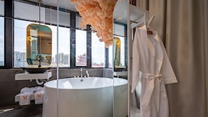 A modern bathroom with a large bathtub, a vanity with a mirror, and a robe hanging on a rack. - Midas Hotel (Ho Chi Minh City)