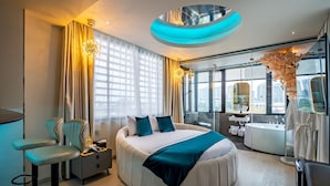 A modern hotel room with a large bed, a sitting area with a chair, a desk, and a bathroom with a bathtub and a mirror. - Midas Hotel (Ho Chi Minh City)