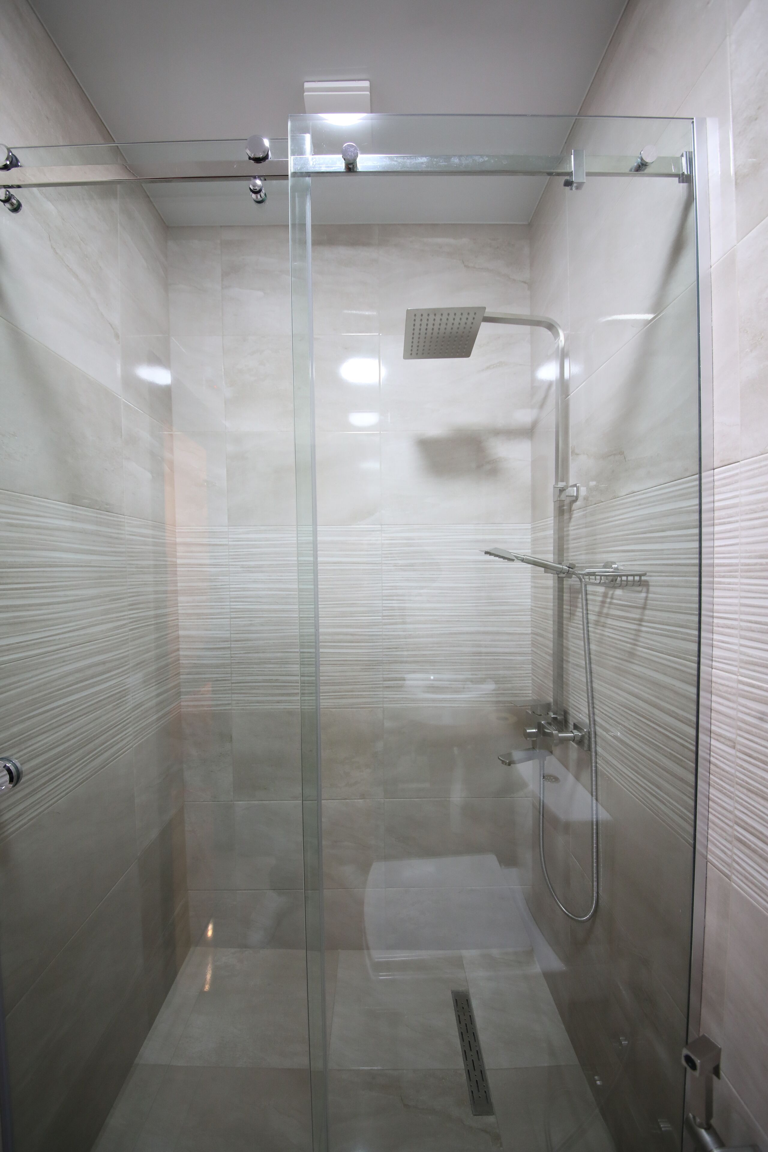 Cabina de ducha con paredes de vidrio, un cabezal de ducha de mano y un grifo instalado en la pared.
