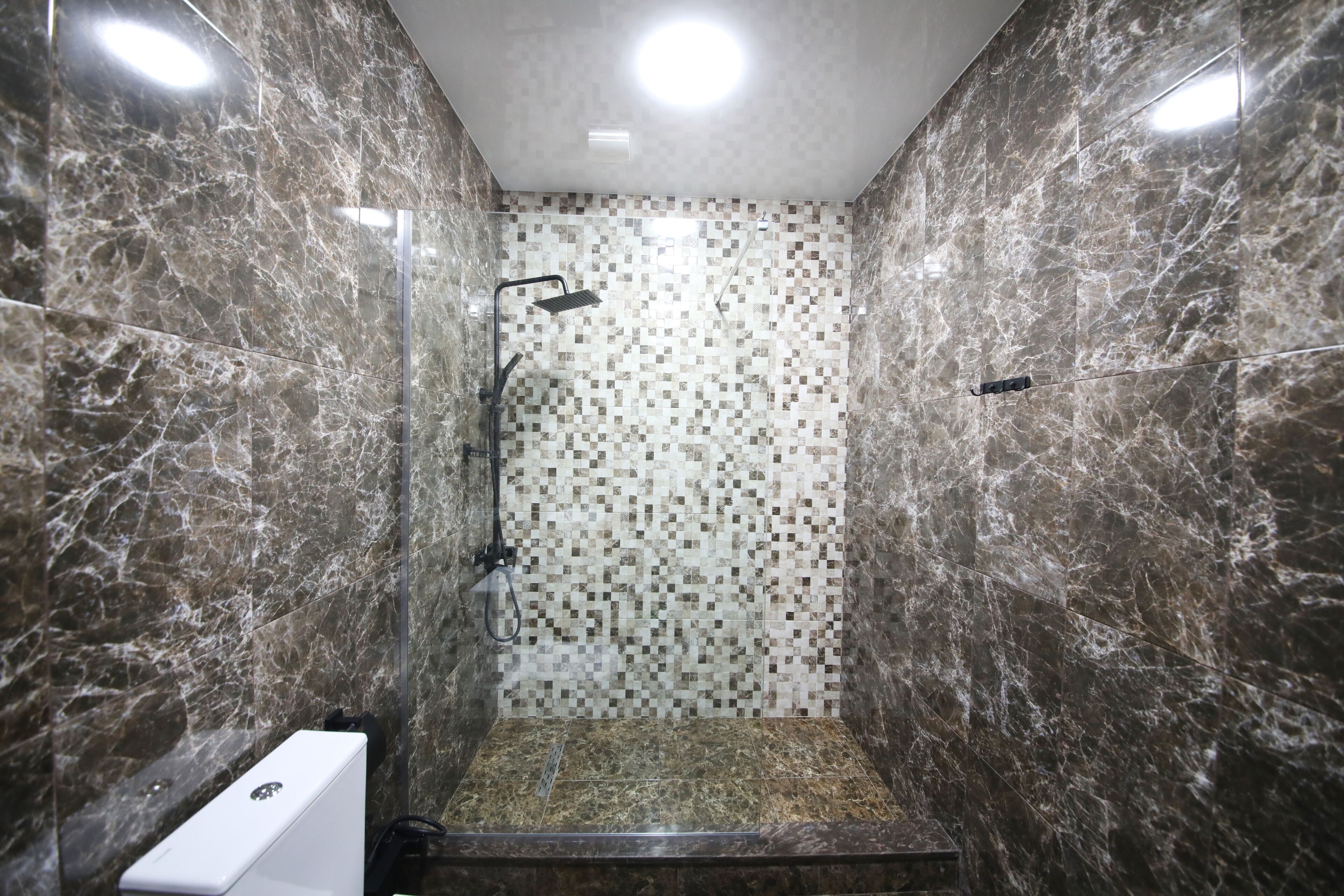 Um chuveiro moderno com porta de vidro, parede com mosaico de azulejos e piso de mármore.
