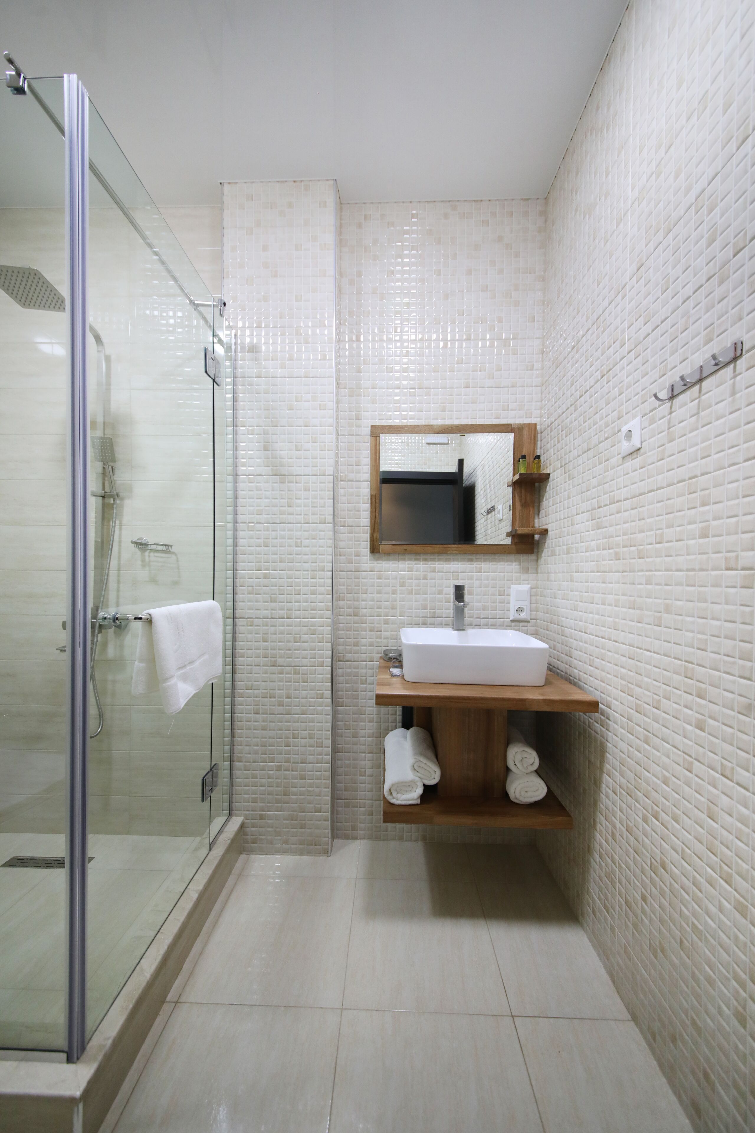 A modern bathroom with a glass-enclosed shower, a white sink with a wooden vanity, and a tiled backsplash.
