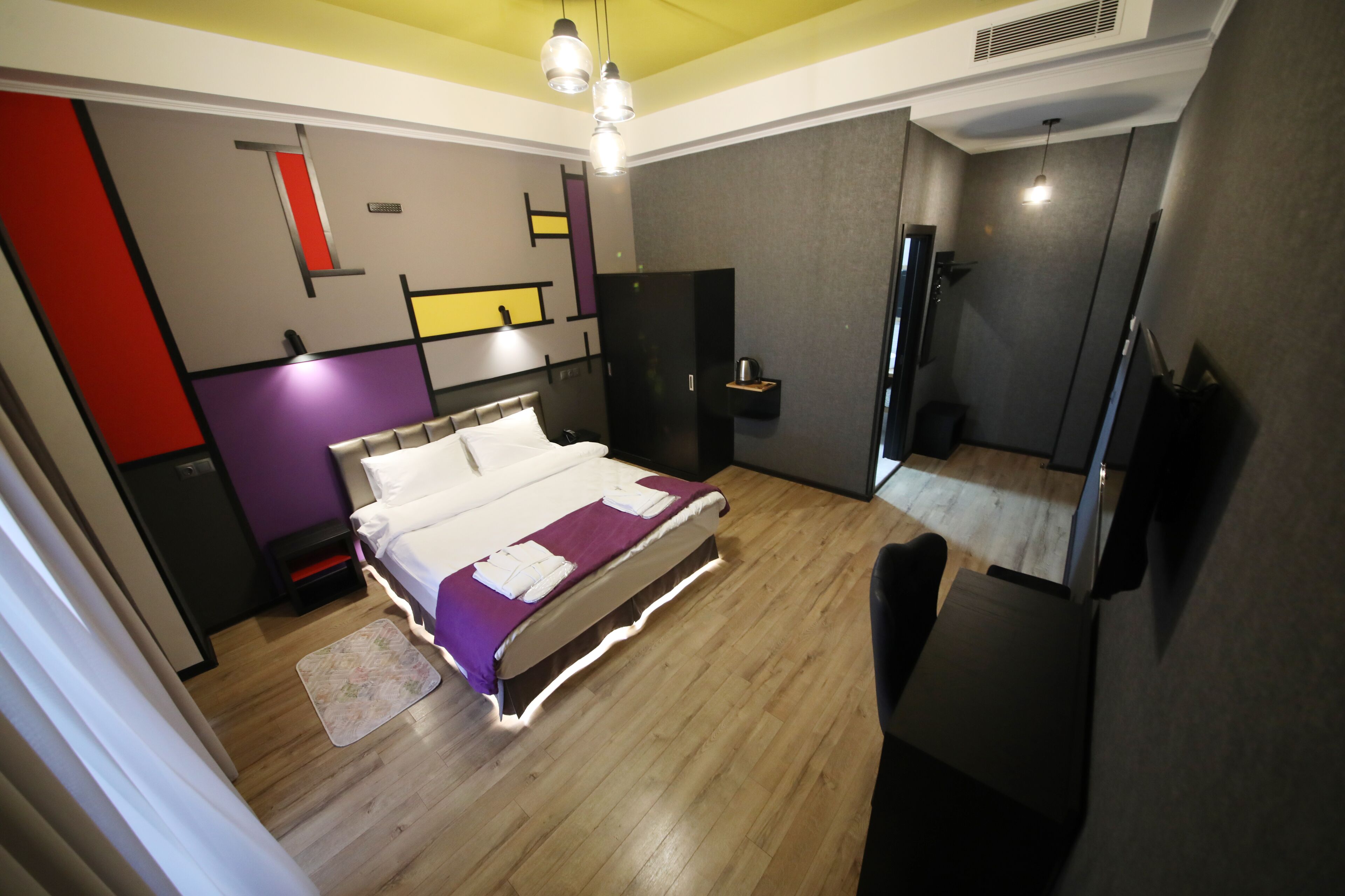 A modern bedroom with a wooden floor, a bed with a purple and white bedspread, a bedside table, and a wardrobe.