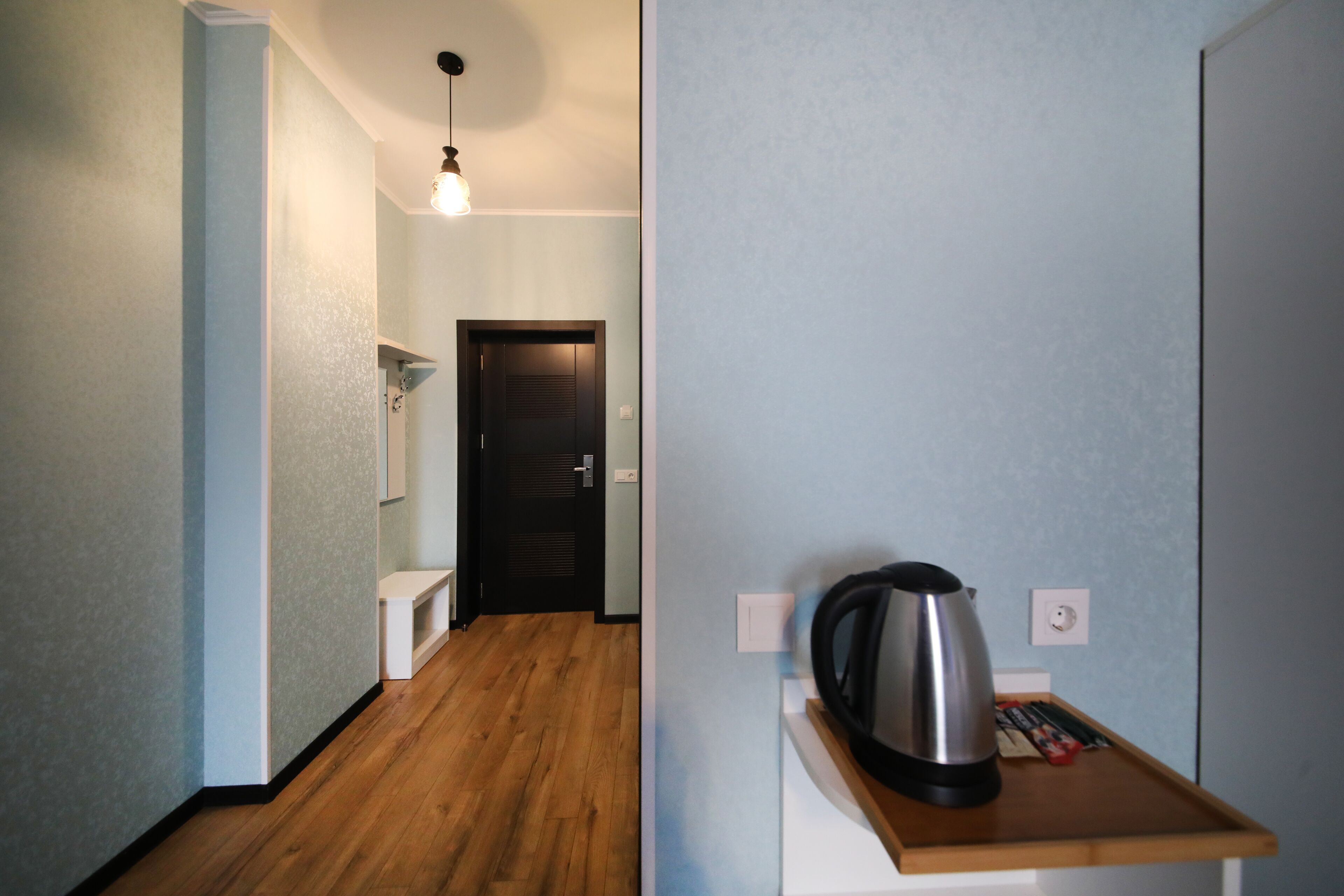 A hallway with a wooden floor, a white bench, a kettle, and a door.