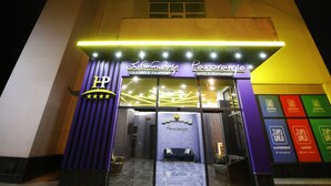 Entrada de hotel com letreiro de neon, escadaria e uma área de recepção visível.