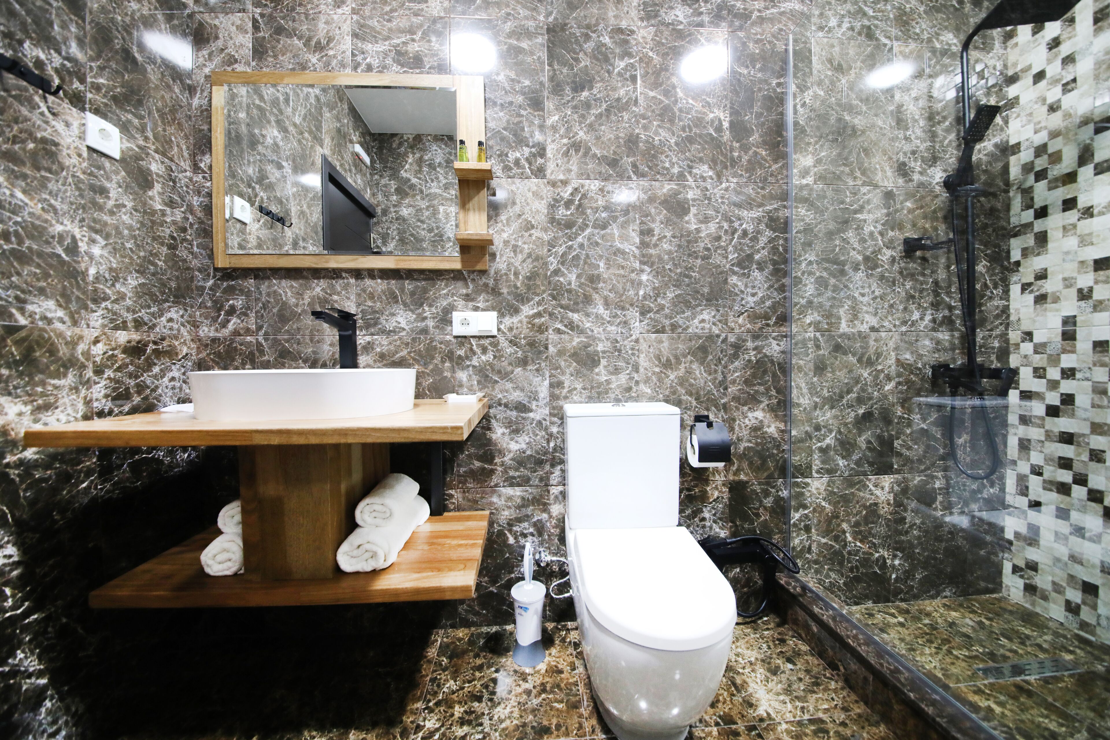 A modern bathroom with a marble sink, wooden vanity, white toilet, and a glass shower enclosure.