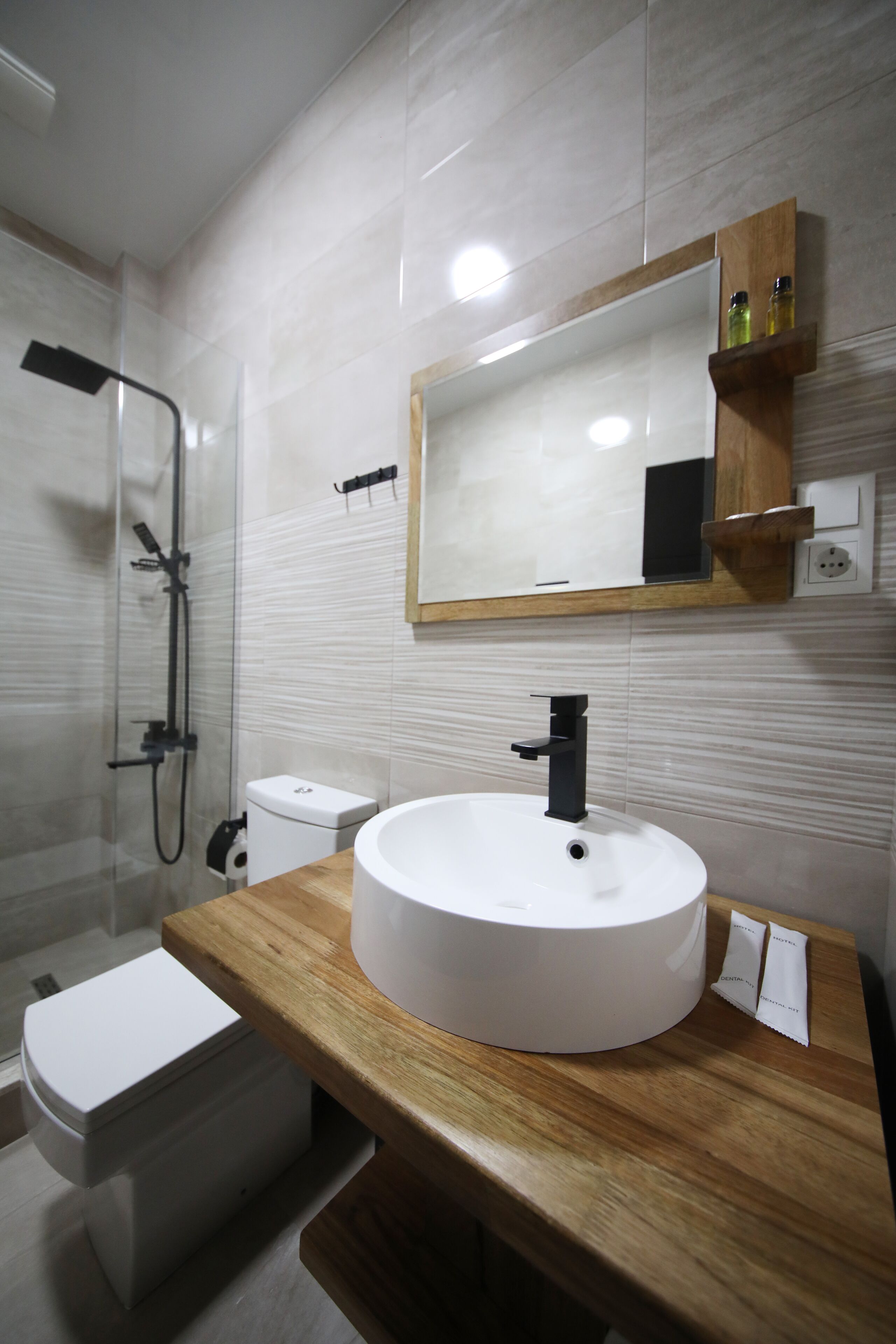 A modern bathroom with a round white sink, a wooden countertop, a mirror, and a shower enclosure.
