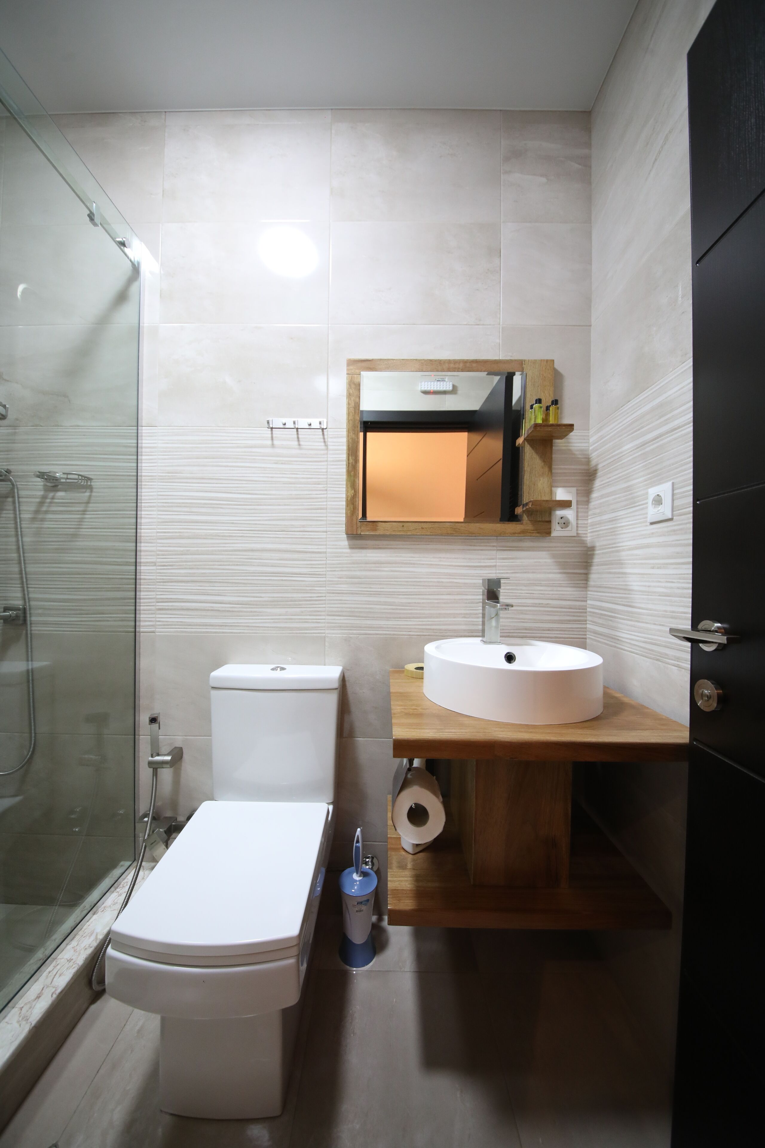 A modern bathroom with a glass shower enclosure, a white toilet, a wooden vanity with a sink, and a mirror above the sink.