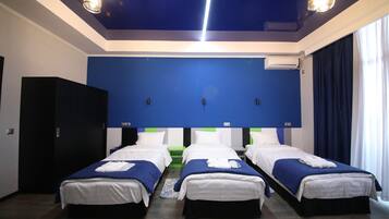 A hotel room with three single beds, a wardrobe, a ceiling light fixture, and a window with curtains.