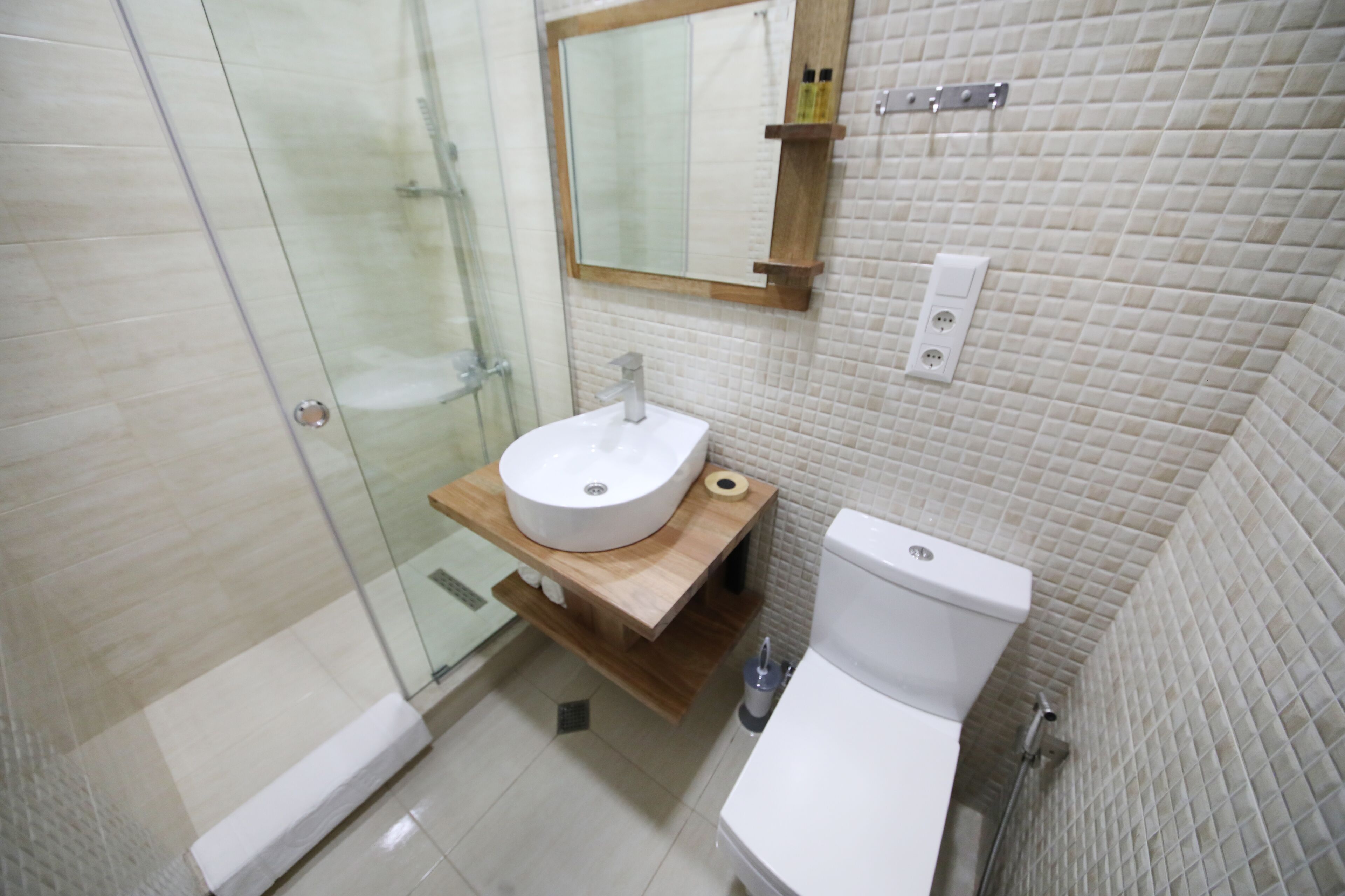 Un baño moderno con cabina de ducha de vidrio, tocador de madera con lavamanos y un inodoro.