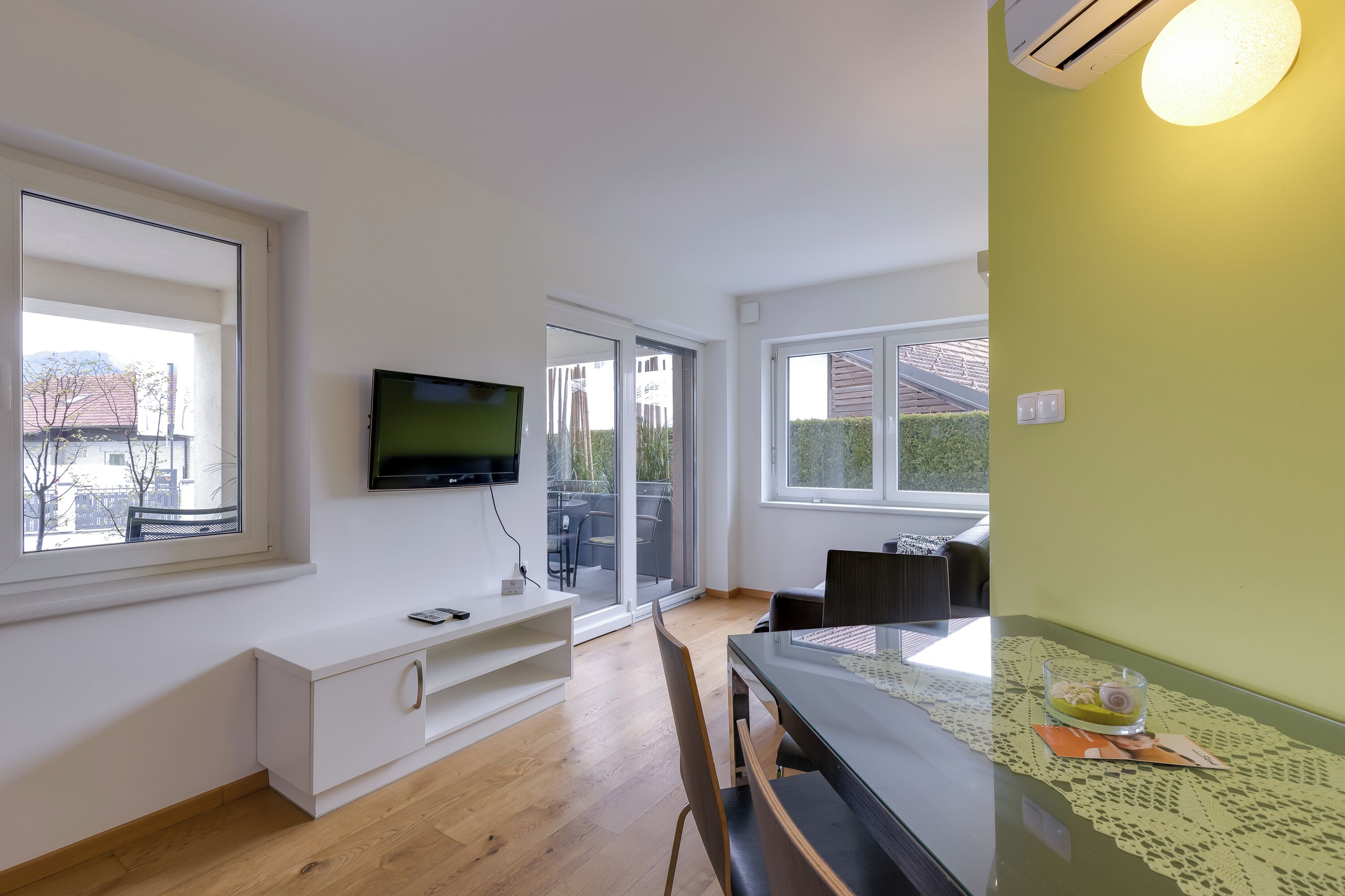 A modern living room with a flat-screen TV, a dining table, and a sofa.