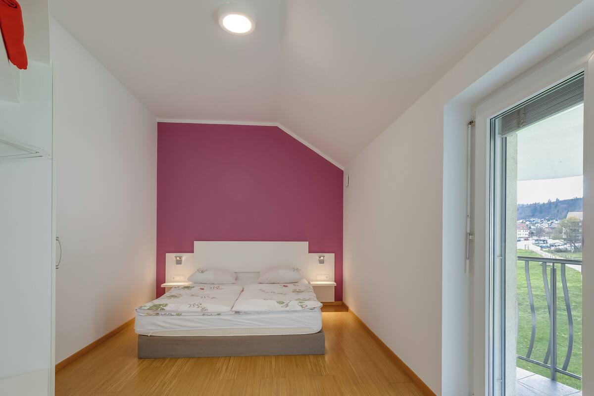 Une chambre à coucher avec un lit, une table de chevet, une fenêtre et une vue sur l’extérieur.
