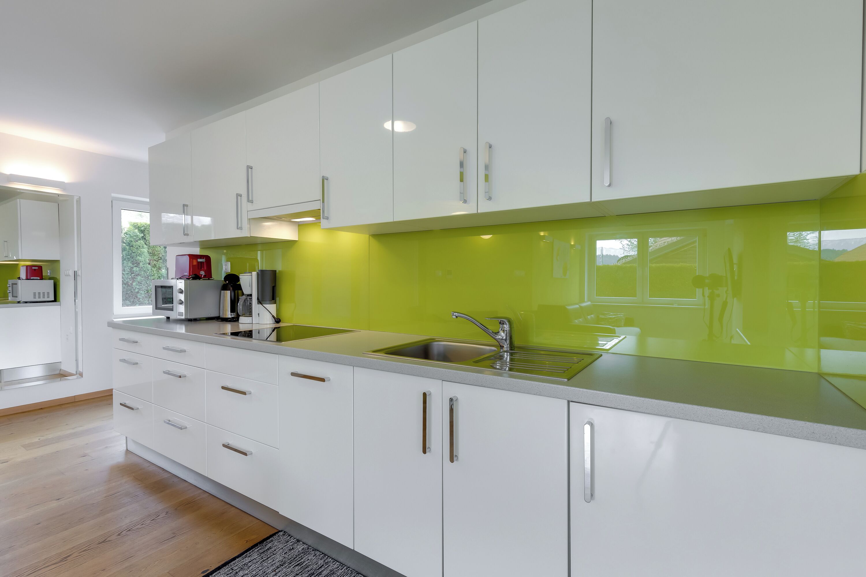 A modern kitchen with white cabinets, a green backsplash, and stainless steel appliances.
