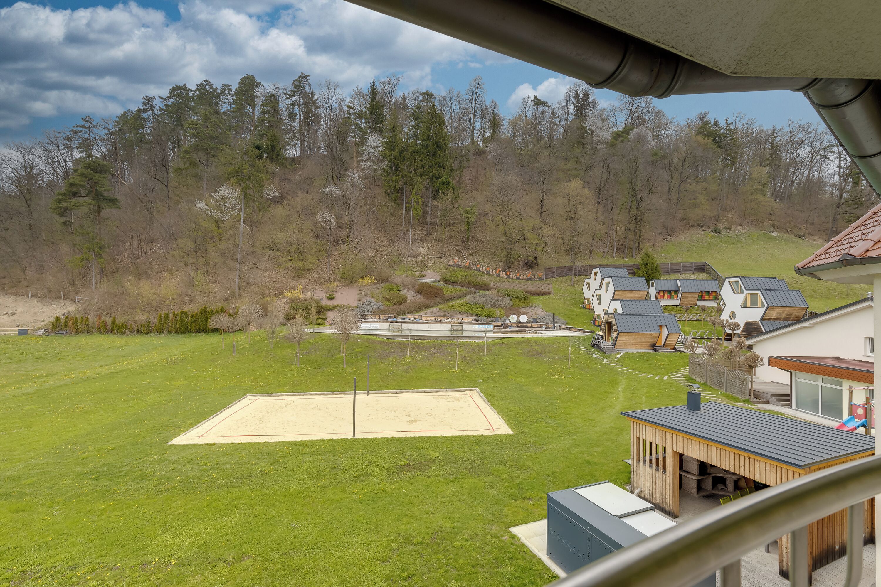 A residential area with a large open grassy field, a tennis court, and several modern houses with unique architectural designs.