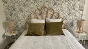A bed with a white textured bedspread, two green pillows, and a wooden headboard. There are two bedside tables with lamps and a wall with a leafy pattern. - Clos des Chardons - Le Jardin (Saint-Aignan)