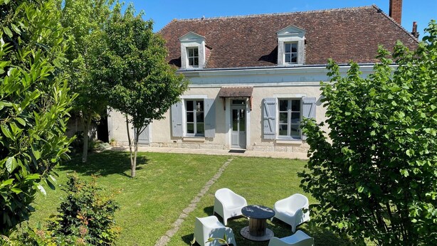 A two-story house with a tiled roof, a small balcony, and a front door. There is a lawn with a seating area and a tree in the foreground. - Clos des Chardons - Le Jardin (Saint-Aignan)
