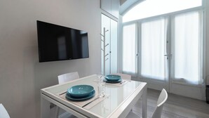 A modern dining area with a white table, blue plates, and a glass of water. A flat-screen TV is mounted on the wall above the table. - Italianway Easy - Naviglio Pavese 6 (Milan)