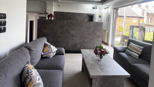 Ein modernes Wohnzimmer mit einer grauen Sofagarnitur, einem zentralen Couchtisch und Blick ins Freie.