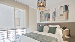 Une chambre moderne avec un grand lit, un balcon, des œuvres d’art abstraites au mur et une suspension lumineuse.