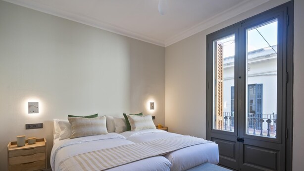 A bedroom with a bed, bedside tables, a bench, and a large window with a view of the outside.