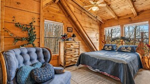 Quarto de cabana de tronco com cama, poltrona, cômoda e ventilador de teto.