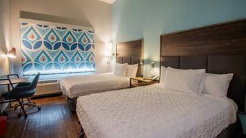 A hotel room with two beds, a desk, a chair, and a patterned wall.