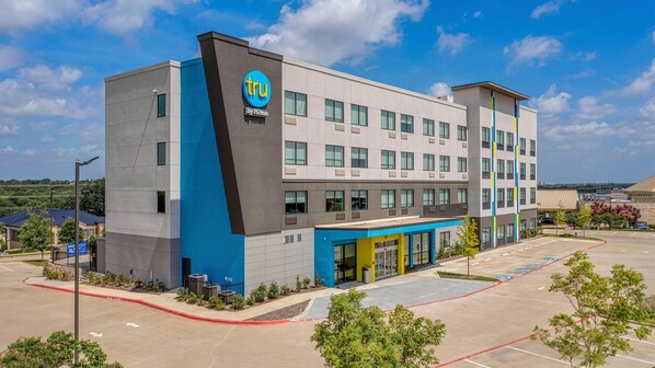 A modern hotel building with a prominent logo, a parking lot, and a clear sky. - Tru By Hilton Mckinney (McKinney)
