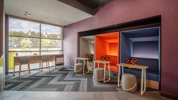 A modern lounge area with seating, tables, and a large window providing a view of the outdoors.