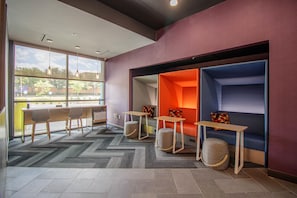 A modern lounge area with seating, tables, and a large window providing a view of the outdoors. - Tru By Hilton Mckinney (McKinney)