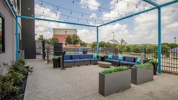 An outdoor seating area with a blue metal frame, a sofa, planters, and a paved floor.