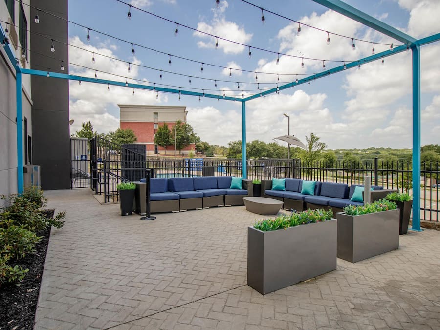 Un espace extérieur aménagé avec une structure en métal bleu, un canapé, des jardinières et un sol pavé.