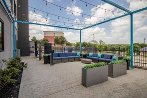 Un espacio de estar al aire libre con estructura metálica azul, un sofá, macetas y suelo empedrado.