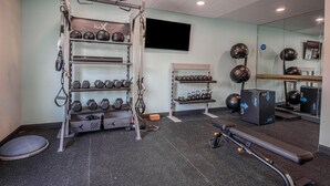 Un gimnasio con barra de dominadas, mancuernas, kettlebells, banco y espejo.