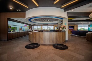 A hotel reception area with a central counter, seating area, and a view of the outside. - Tru By Hilton Mckinney (McKinney)