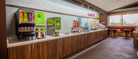 A yogurt and oatmeal dispenser, a coffee machine, and a seating area with tables and chairs.