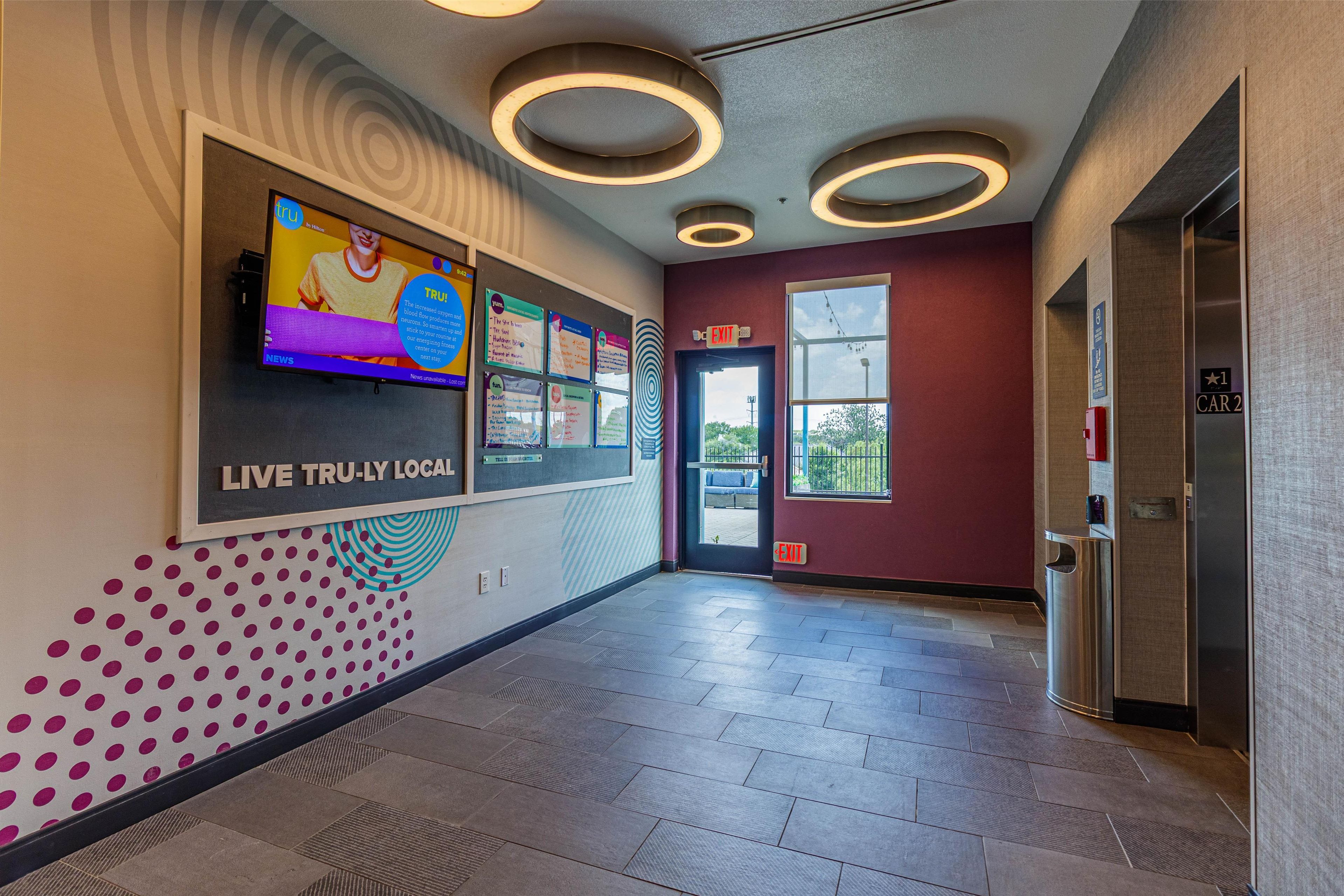A hallway with a TV screen, exit signs, and a trash can.