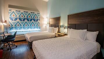 A hotel room with two beds, a desk, a chair, and a patterned wall.